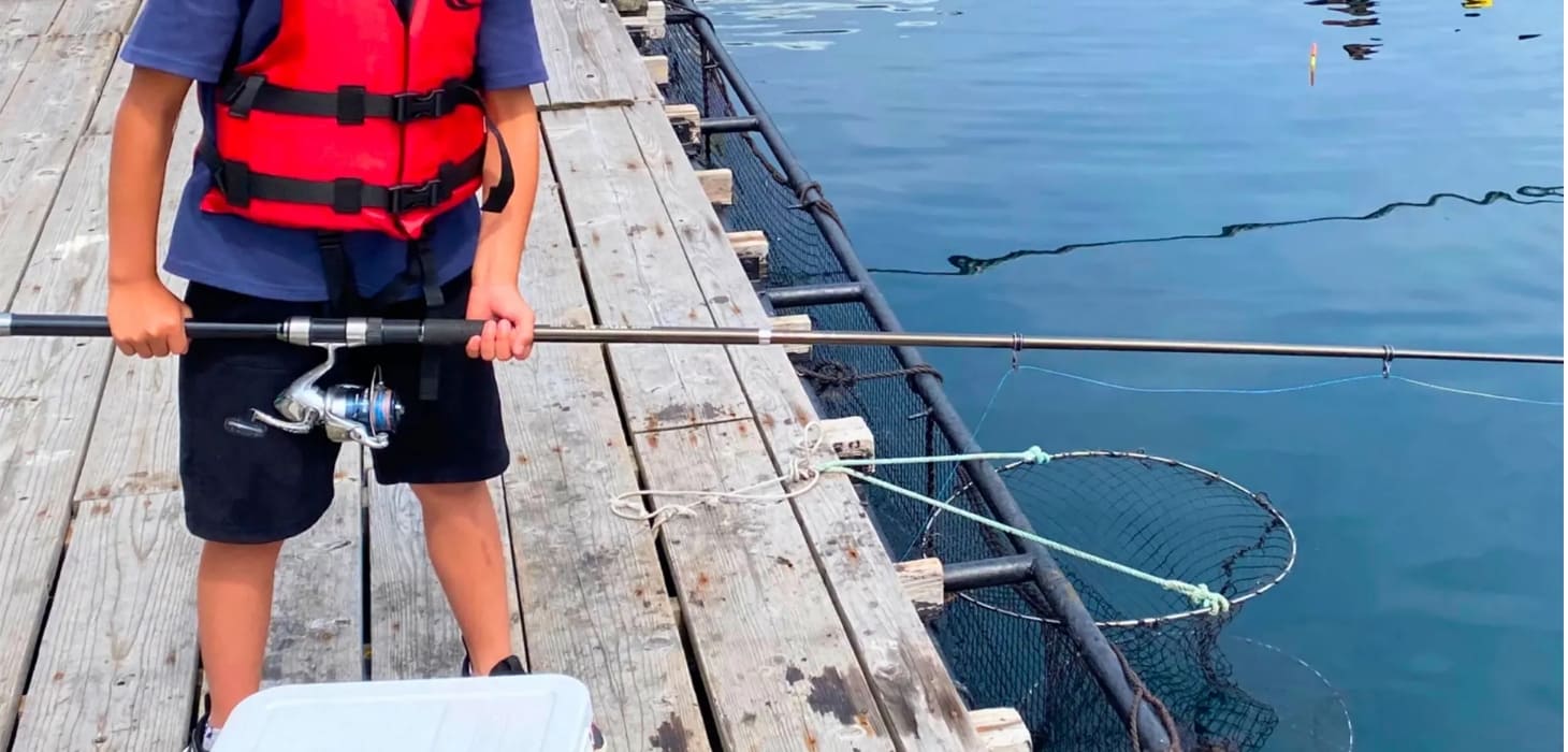 [写真] ライフジャケットを着用し、桟橋の上で真剣に釣り糸を垂らす子供の様子