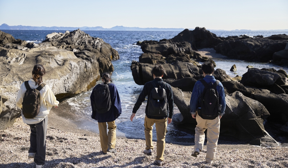 [写真] 岩場の続く海岸線を散策する4人の男女