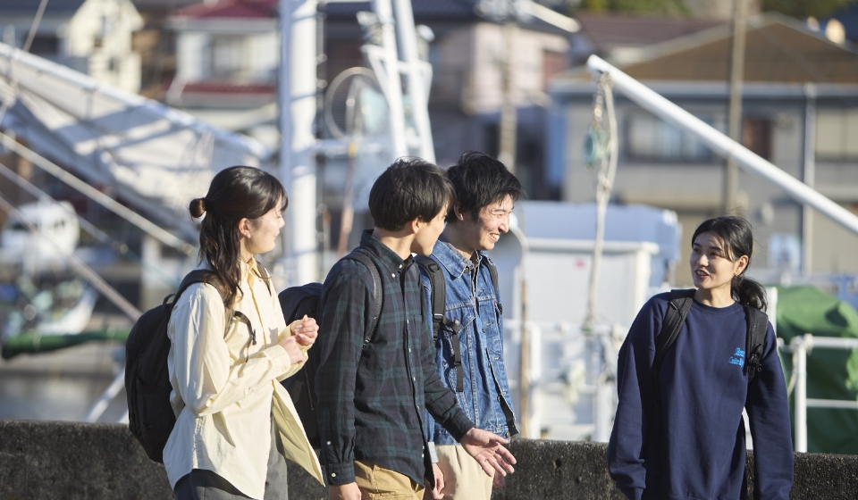 [写真] 漁港を背景に楽しそうに談笑しながら歩く4人の様子