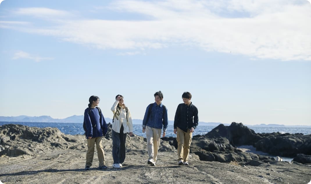 [写真] 青空の下、開放感のある岩場を並んで歩く4人