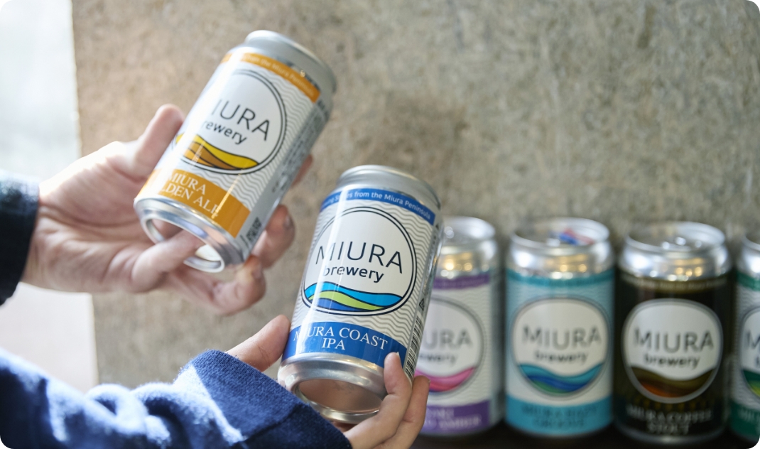 [写真] 「MIURA GOLDEN ALE」や「MIURA COAST IPA」など、色鮮やかなラベルの缶ビールを手に取る様子