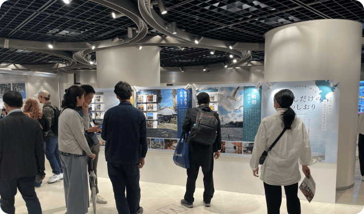 [写真] 展示ブースでパネルを見つめる来場者たち